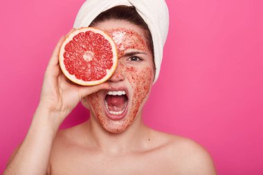 Kızgın yüz ifadesi ile genç kadının portresi, başında beyaz havlu ile banyoda çığlıklar, greyfurt ile gözünü kapamak, yüzünde scrub vardır, evde kozmetik prosedürleri.