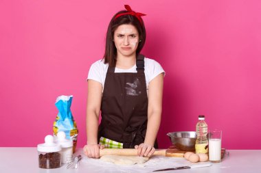 Sevimli ev hanımı veya fırıncı Görüntü yorgun ve üzgün görünüyor, somurtkan dudakları ile duruyor, paskalya için hazırlanıyor hasta ve yorgun, Paskalya kek pişirir, un ile kirli yüzü vardır, pembe arka plan üzerinde izole.
