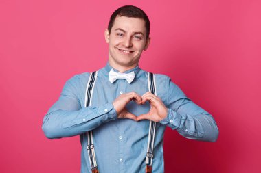 Yakışıklı romantik gülümseyen genç adam portresi göğüs üzerinde kalp işareti yapma ellerini bir araya koyar, memnun ve mutlu görünüyor. İnsanlar, gençlik ve duygu kavramı. Reklam için kopya alanı.