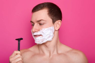 Özenli bakımlı iyi görünümlü genç adam bir elinde siyah jilet tutar, ona doğru bir görünüm verir, bakım prosedürleri yapmak için gidiyor. Reklam için kopya alanı. Bakım, güzellik ve erkeklik kavramı.