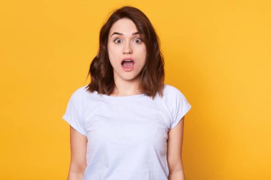 Son haberlerden etkilenen, ağzı açık ve kahverengi gözleri olan, şaşırmış görünen, çok duygusal yüz ifadesi olan ince genç bayan. Reklam için kopya alanı.