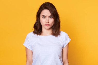 Yüzünde hayal kırıklığına uğramış bir görünüme sahip çekici sefil kızın portresi, doğrudan kameraya bakıyor. Duygusal büyüleyici modeli sarı arka plan üzerinde izole pozlar. İnsanlar ve duygular kavramı.