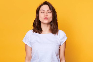 Genç manyetik esmer kadın, gözleri kapalı, dudaklarını dışarı çıkarıyor, öpüşme işareti yapıyor, romantik görünüyor. İnce ve enerjik modelin barışçıl bir yüz ifadesi vardır. Duygusal durum kavramı.