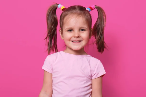 Close-up portret van vrolijke lieve kleine meid met grappige Pigtails, lachend oprecht, direct kijken naar de camera, rechtlijnig, met kleurrijke scrunchies. Ruimte voor advertentie kopiëren. — Stockfoto