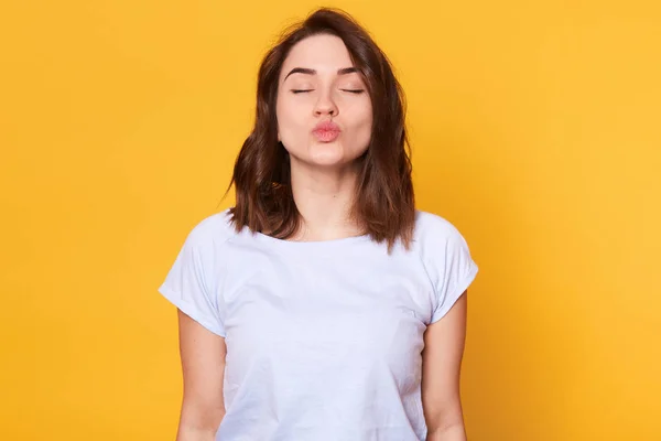 Jovem morena magnética de pé com os olhos fechados, salientando os lábios, fazendo sinal de beijo, parece romântico. Modelo energético esbelto tem expressão facial pacífica. Conceito de estado emocional . — Fotografia de Stock