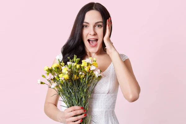 분홍색 배경 위에 고립 된 젊은 아가씨가 깜짝 놀라 입을 크게 열고 봄 꽃다발을 들고 행복해 보입니다. 광고의 공간을 복사합니다. 사람과 감정 개념. — 스톡 사진