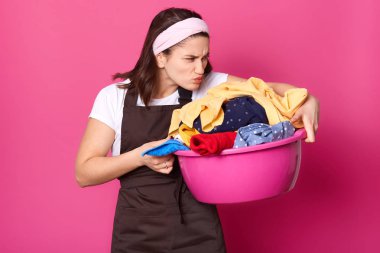Ev işleri yapan, kirli çamaşırları koklayan, onları yıkayan, iğrenç bir yüz ifadesine sahip, çamaşır yıkama işleminden nefret eden genç ev kadınlarının kapalı çekimleri. Ev işleri ve ev işleri kavramı.