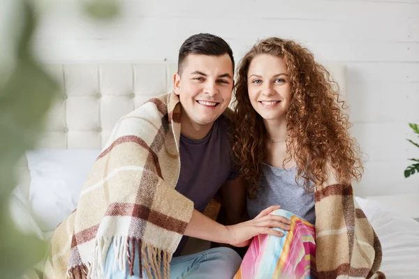 Close up retrato de casal romântico apaixonado sentado sob xadrez quente no quarto, abraçar uns aos outros e ter expressões faciais positivas, desfrutar de união, vestir-se casualmente, olhando para a câmera . — Fotografia de Stock