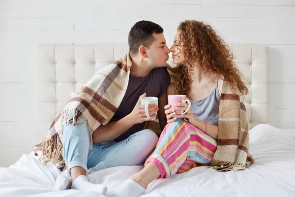 Indoor tiro de mulher feliz e do sexo masculino têm relacionamentos românticos, beber café ou chá, coberto com xadrez no quarto. Casal romântico gostando de passar o lazer juntos. Conceito de relação . — Fotografia de Stock