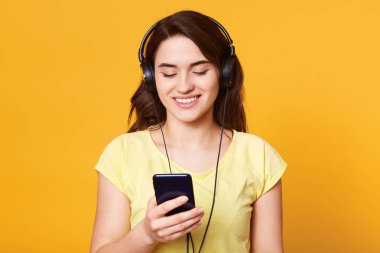Rahat gömlek güzel koyu saçlı kız Görüntü favori müzik ile rahatlatır. Onun akıllı telefon tutan scaucasian kadın kapalı portre ve çalıştırmak için müzik seçer, stüdyo duvarına karşı model.