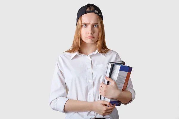 Young student has bad result of exam. Schoolgirl stands isolated over white background, girl studies at school, holding paper folders in hands, wearing blouse. Education and teenager concept.