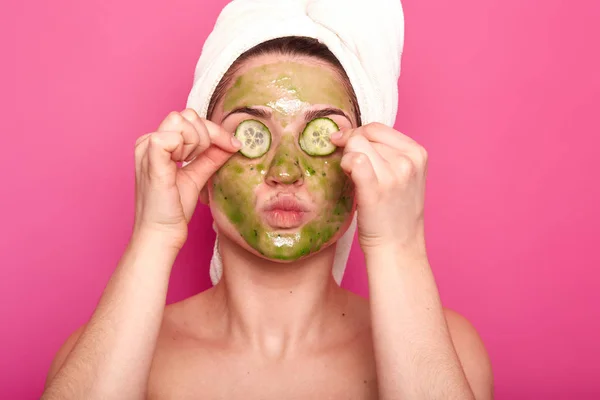 Plan intérieur de jeune femme séduisante avec masque vert sur son visage mettant des parties de concombre sur ses yeux, faisant saillie sur ses lèvres, ayant un corps nu, porte une serviette blanche sur ses cheveux, temps de spa relaxant . — Photo