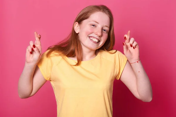 Πορτρέτο των ευχών νεαρή γυναίκα σε casual κίτρινο t sirt, με καστανά μαλλιά, διασχίζοντας τα δάχτυλά της, ελπίζει πριν από σημαντικό γεγονός, απομονώνονται σε ροζ φόντο. Γλώσσα του σώματος, τα συναισθήματα των ανθρώπων έννοια. — Φωτογραφία Αρχείου