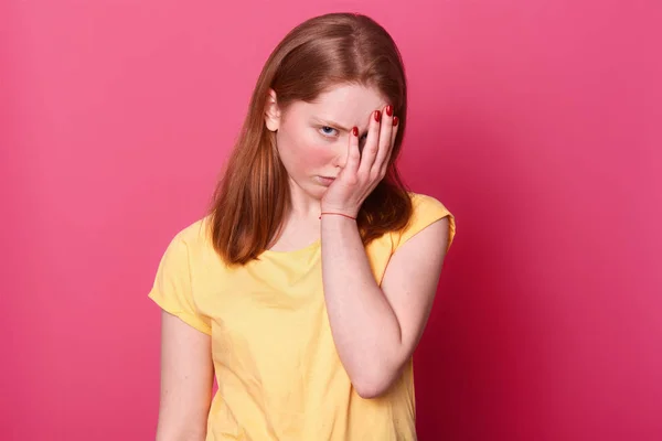 Cierre de retrato de joven hermosa estudiante mujer, cubre la cara con la mano, estar cansado después de la escuela, tiene un montón de tareas, quiere relajarse, aislado sobre fondo rosa. Concepto de cansancio . — Foto de Stock