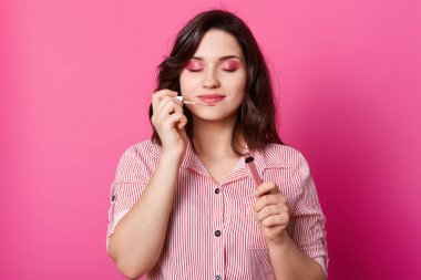 Güzel esmer kadın tutan ve kokulu tatlı dudaklar parlak portresi kadar yakın, kapalı gözleri ve parlak makyaj ile poz, bluz giyen, gül stüdyo duvarına karşı ayakta. Güzellik konsepti.