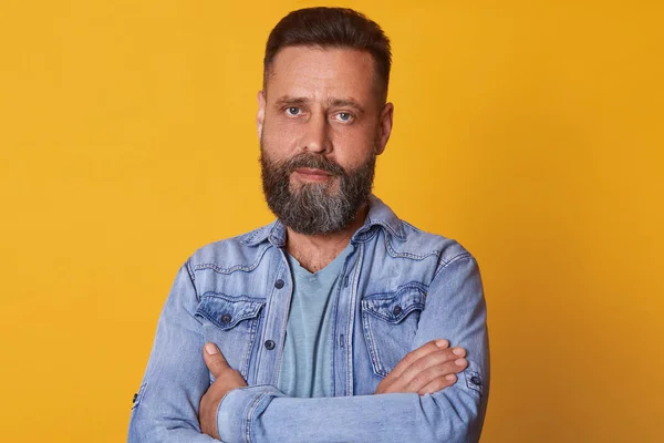Indoor studio close up portrait of strong charismatic bearded blue eyed man standing with folded arms isolated over bright yellow background in studio, having confident, calm facial expression. — Stock Photo, Image