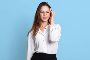 Stresli çekici genç ofis çalışanı stüdyoda açık mavi arka plan üzerinde izole ayakta, el ile onun şakak dokunmadan, ağrı hissi, baş ağrısı olan, zor iş gününden sonra yorgun görünüyor.