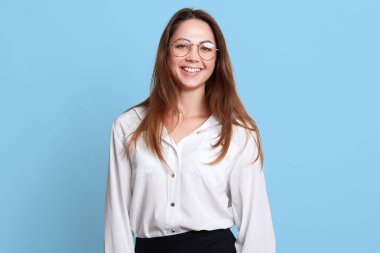 Başarılı neşeli yönetici açık mavi arka plan üzerinde izole ayakta Kapalı stüdyo çekim, olumlu yüz ifadesi olan, resmi ofis giyim ve gözlük giyiyor. Ofis çalışma konsepti.