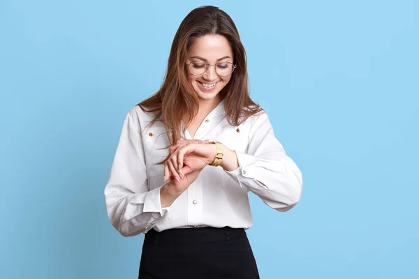 Studio girato di felice sorridente bella bruna giovane donna in abiti formali in piedi e controllare il tempo, essendo di fretta, ha importante incontro, isolato su sfondo blu. Concetto aziendale . — Foto Stock