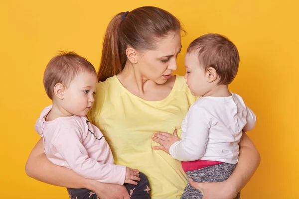 Bilde av mor med sine søte barn, poserer i studio. Mamma og jenter, tvillinger, kledd som venner, forteller om morsdagen. Små barn hører på mamma og klemmer henne . – stockfoto