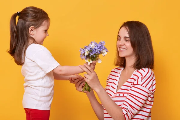 Selamat hari ibu! Anak perempuan mengucapkan selamat kepada ibu dan memberinya karangan bunga. Ibu memakai baju bergaris-garis dan gadis kecil terlihat bahagia. Keluarga, liburan, kebersamaan dan konsep kebahagiaan . — Stok Foto
