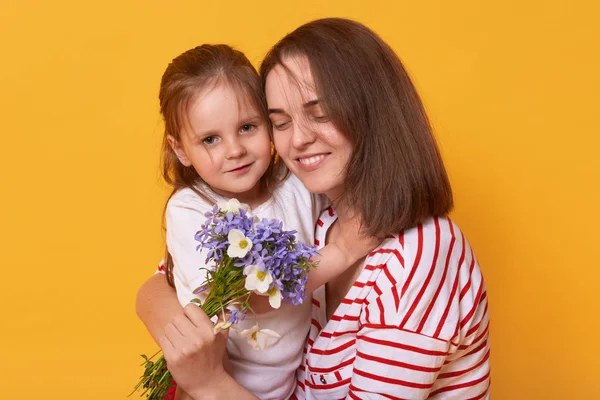 Photo of happy mother and kid. Affectionate female holds on tight her little charming daughter. Cute child gives bouguet of flowers to her mummy, congratulates with Mother's Day! Happyness concept. — Stock Photo, Image