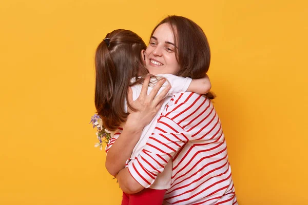 Mother and doughter hug each other with love, little cute girl wishes joy her mom on holiday, pose isolated over yellow studio background, family express happyness and gladness. Happy mother's day! — Stock Photo, Image