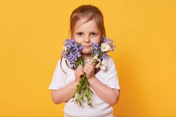 Ritratto di bambina con mazzo di fiori da giardino isolato su sfondo giallo studio, pronto a congratularsi con la sua mamma affettuosa con la festa della mamma. Famiglia, felicità e concetto di vacanza — Foto Stock