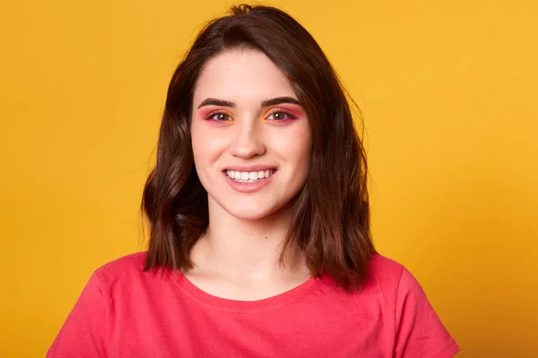 Närbild porträtt av vackra kaukasiska ung kvinna med rosa och orange glamour smink och Toothy leende, har modellen glad ansiktsuttryck, klädd nonchalant, poserar isolerade på gul bakgrund. — Stockfoto