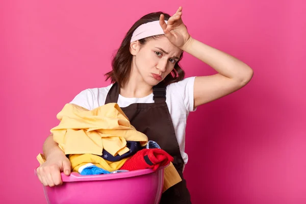 Mujer cansada y trabajadora con la cara fruncida tocándose la frente con la mano, limpiando el sudor, haciendo muchas tareas domésticas, sacando ropa limpia de la lavandería, mirando directamente a la cámara con tristeza . —  Fotos de Stock