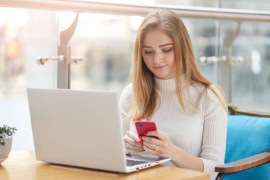 Güzel genç sarışın üniversite öğrencisi kafede tur üst önünde mavi kanepede oturan Fotoğraf, mola ederken e-posta cheching, rahat giyinmiş, uzun sraight saçları vardır, sınıflar için hazırlanıyor.