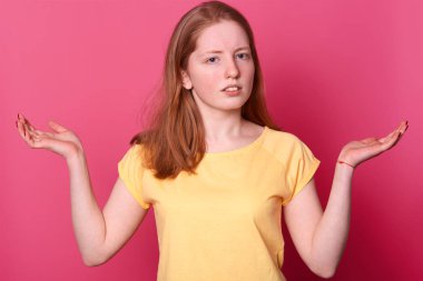 Sarı t shirt şaşkın tahriş şok genç kadın Portresi, düz kahverengi saçlı, fotoğraf stüdyosunda pembe arka plan izole elleri yayılıyor. İnsanlar samimi duygular, yaşam tarzı kavramı.