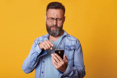 Çekici görünümü, koyu saçlı ve sakallı orta yaşlı bir adamın stüdyo çekimi, rahat giyinmiş rahat görüntülü arama için modern akıllı telefon kullanır, konuşma, işaret parmağı ile pnone ekrana işaret.