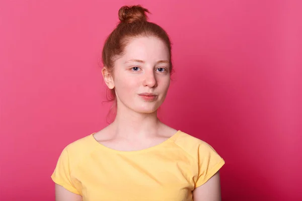 Close up retrato de uma jovem com um monte de cabelo, vestindo camiseta casual amarela. Bonita fêmea posando dentro de casa isolada sobre fundo rosa. Copiar espaço para o seu texto de publicidade ou promoção . — Fotografia de Stock
