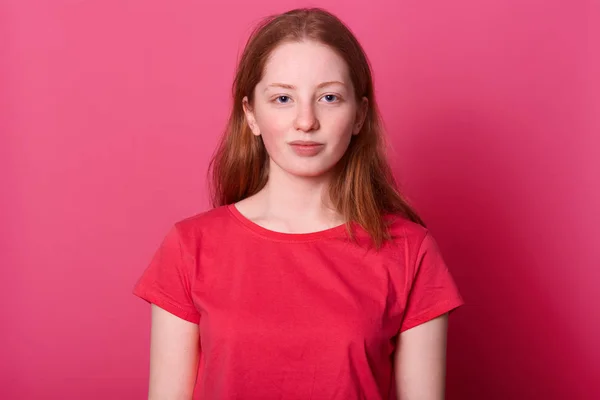 Retrato de meia lengh de jovem estudante olhadas femininas com expressão facial calma na câmera, vestindo camisa casual vermelha, tem cabelos castanhos lisos longos e belos olhos azuis, isolados sobre fundo rosa — Fotografia de Stock
