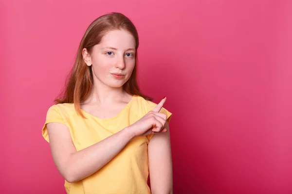 Portrait of girl in yellow casual clothes pointing index finger aside isolated on pink wall background in studio. People sincere emotions lifestyle concept. Copy space for advertisment and promotion. — Stock Photo, Image