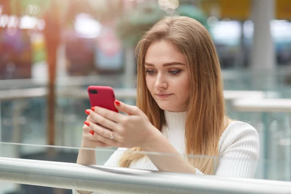 Beltéri shot figyelmes súlyos, tisztességes hajú lány gazdaság okos telefon GER kezében, nézte a képernyőn, figyelembe fotó beltéri, így tegye a szociális hálózati oldalak. Emberek és technológiai koncepció. — Stock Fotó