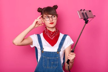 Genç manyetik iyi görünümlü kadın el ile selfie sopa tutan portre, baş dokunmadan, kamera bakarak, fotoğraf yapma, stüdyoda pembe arka plan üzerinde izole poz. Sosyal medya kavramı.