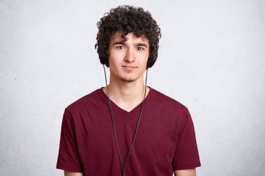 Kıvırcık başlı adam portresi, rahat bordo t shirt giyen, kulaklık müzik dinlerken stüdyoda poz, kamera bakarak, hoş bir yüz ifadesi vardır. Promosyon için kopya alanı