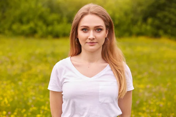 Gros plan portrait de belle jeune femme caucasienne reposant dans la nature, pose isolée sur fond de prairie, jolie femme regardant directement la caméra avec une expression faciale agréable. Concept jeunesse . — Photo