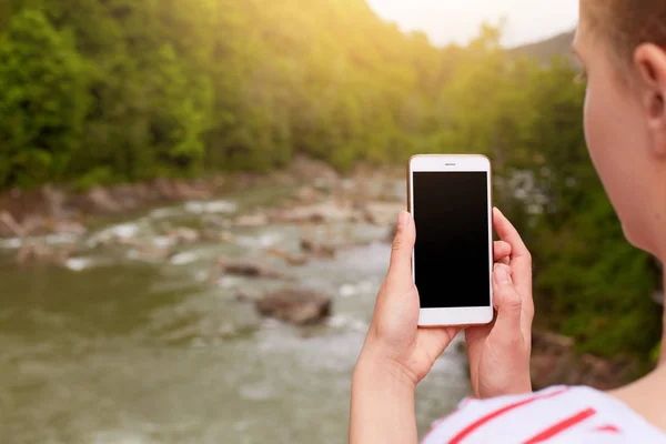Smartphone w ręce kobiety, fotograf sprawia, że zdjęcie pięknej przyrody, pusty ekran na urządzeniu. Zdjęcie górskiej rzeki i lasu, kobiece strzelanie wideo do delegowania na portalach społecznościowych. — Zdjęcie stockowe