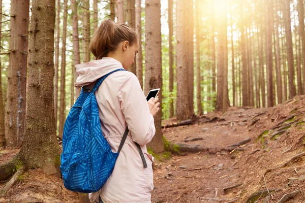 Obraz batůžkáře, který se snaží najít svou cestu, pomocí mobilního telefonu v lese, ženský chodí na procházku v jarní sezóně, atraktivní dáma oblečená nenuceně. Cestování a mít koncept dobrodružství. — Stock fotografie