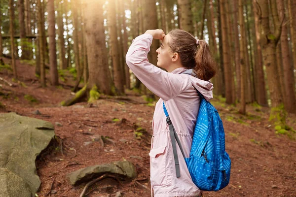 Colpo all'aperto di esploratore entusiasta che si tocca la fronte con mano, coprendo gli occhi dai raggi del sole, guardando lontano, godendo di viaggio, alla ricerca di itinerario di viaggio. Concetto di persone e avventure . — Foto Stock