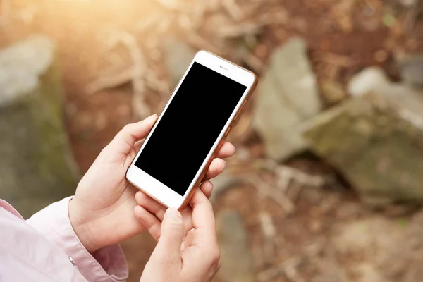 Shot of smartphone be held in both hands in front of stones and forest plants, screen of device is block, mobile phone is out of charge, no connection. People and modern technologies concept. — Stock Photo, Image