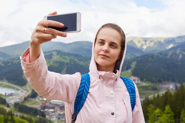 Aufnahme von hübschen jungen Touristin macht Selfie in den Bergen, Frau Reisende im Freien vor schöner Landschaft fotografiert. Reisen, Lifestyle, Abenteuer und Aktivurlaub. — Stockfoto