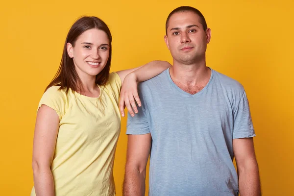 Estúdio tiro de feliz casal jovem positivo olhando e sorrindo para a câmera, menina vestindo camiseta amarela de pé com a mão no homem mais velho, atraente masculino vestido cinza camisa casual tem satisfeito expressar — Fotografia de Stock