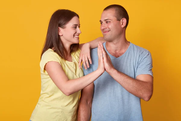 Indoor tiro de cara feliz e alegre senhora caucasiana tocando com palmas contra fundo amarelo, casal apaixonado de pé perto um do outro e olhando gentilmente um para o outro, celebrando saccess . — Fotografia de Stock