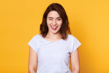 Kamerada doğrudan görünümlü komik oynak siyah saçlı kız portre, bir göz kapanış, dilin ucu gösteren, yüksek ruhlar olmak, giysi rahat öğe giyiyor. İnsanlar ve duygular kavramı.