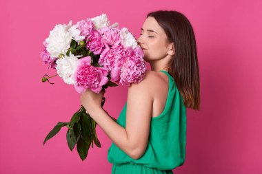 Beyaz ve gül peonies, büyük buket ile çekici kadın tutan güzel esmer kız profil çekim, kadın çiçekler kokuyor, yeşil Sundress giyinmiş, sarı pembe arka plan karşı poz.