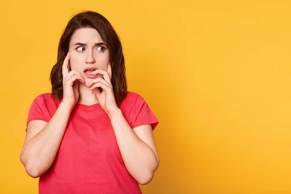 Mujer joven nerviosa preocupada mirando a un lado, tocándose la boca y la cara con ambas manos, abriendo la boca, sintiéndose mal, aislada sobre fondo amarillo en el estudio. Copyspace para publicidad . — Foto de Stock